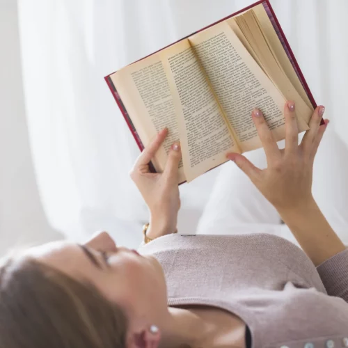 close-up-young-woman-lying-bed-reading-book.opti