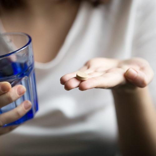 Female hands holding pill and glass of water, woman taking supplements or antibiotic antidepressant painkiller medication to relieve pain headache, contraception side effects concept, close up view